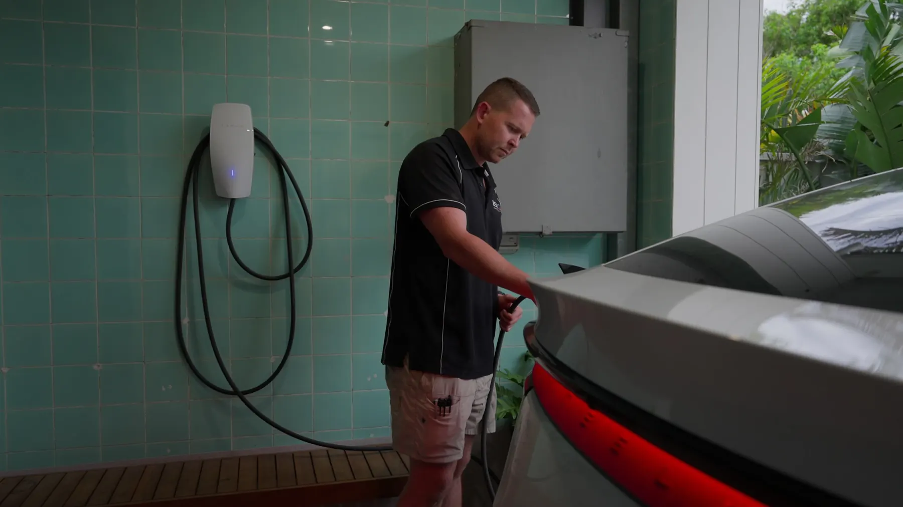 Ben beside an EV wall charger on a teal tiled wall